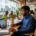 Young Nigerian entrepreneur reviewing funding charts on MacBook in Lagos co-working space, city skyline visible through windows