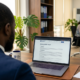 Nigerian business professional signing a compliance document beside a laptop showing a privacy policy page in a bright office